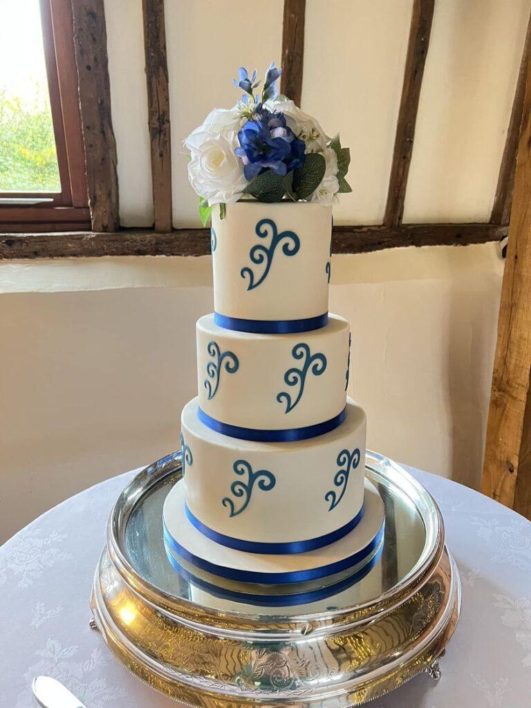 3 tier white wedding cake with blue scroll design and flowers on the top