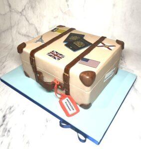 Cream suitcase with brown straps, made from vanilla sponge and raspberry jam. Decorated with flags and passports from edible images.