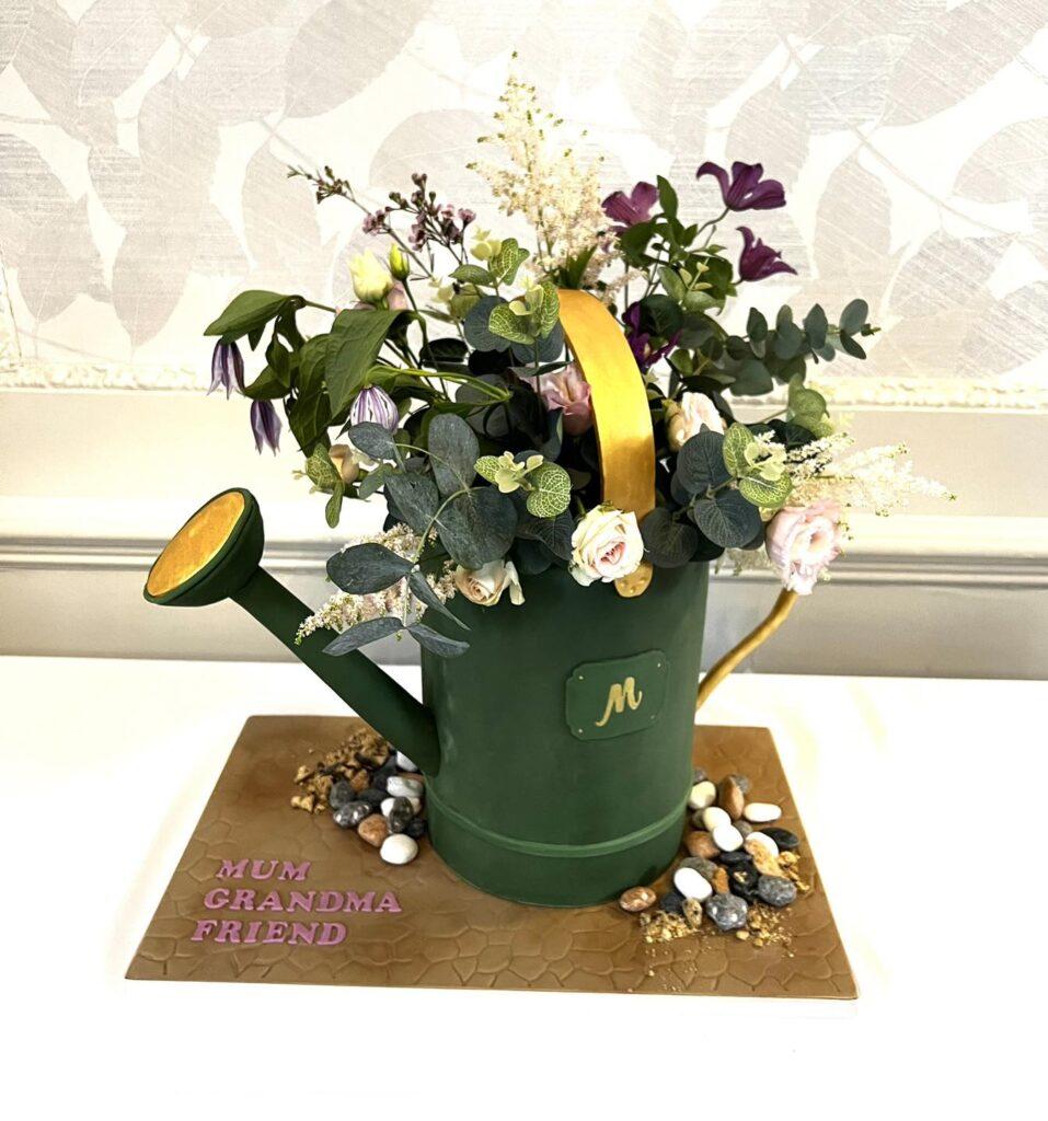 Green watering can cake. A handmade watering can cake. FInished in greem fondant and edged in gold. With fresh flowers.